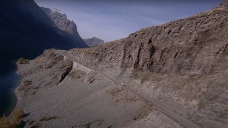 Um carro é visto dirigindo ao longo de uma estrada de montanha remota a partir de uma vista aérea no brilho