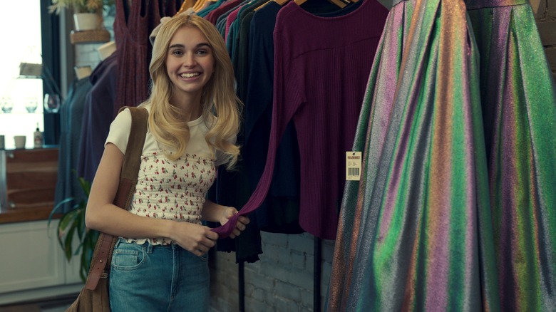 Nikki Roumel's Georgia/Mary smiles next to a rack of clothes in a store in Ginny & Georgia