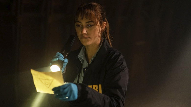 Agent Harker shining a flashlight onto a piece of paper with a symbol on it in Longlegs