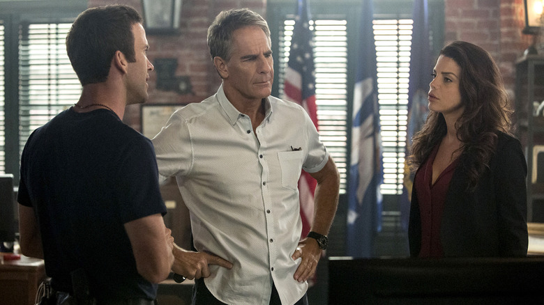 Tanny and Christopher standing around Dwayne in the office in the NCIS: New Orleans episode Escape Plan