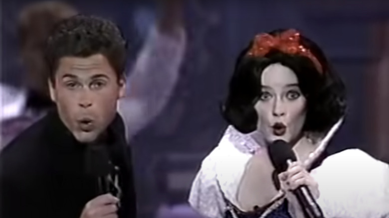 Rob Lowe e uma atriz vestida como Branca de Neve segurando microfones e cantando no palco do Oscar de 1989