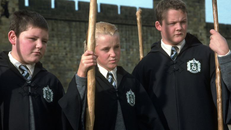 Crabbe and Goyle, flanking Draco Malfoy, each of them holding broomsticks.