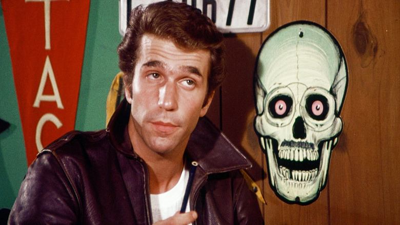 Fonzie parado ao lado de um logotipo do crânio em dias felizes