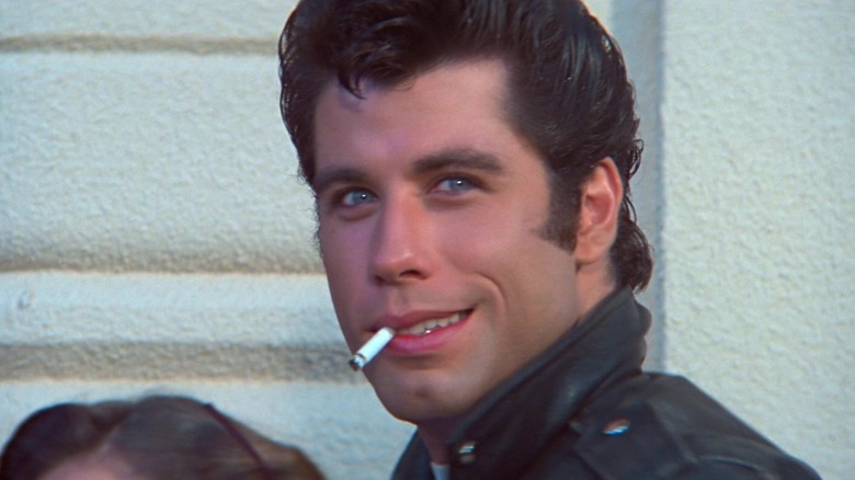 John Travolta as Danny Zuko smiling with a cigarette dangling out of his mouth in Grease