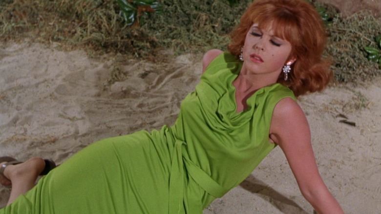 Ginger, in a green dress, acting a death scene on the beach.