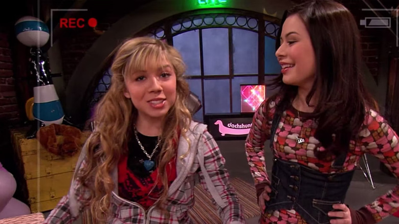 Sam facing the camera while Carly smiles with her hands on her hips in iCarly