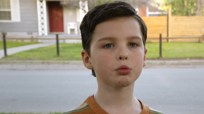 Iain Armitage as Sheldon Cooper standing outside in an orange shirt in Young Sheldon season 1