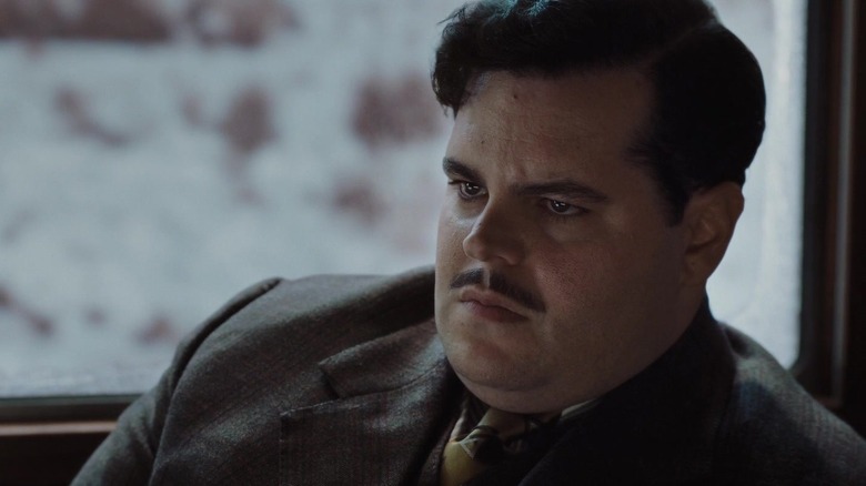 Josh Gad as Hector MacQueen sitting stone-faced in Murder on the Orient Express