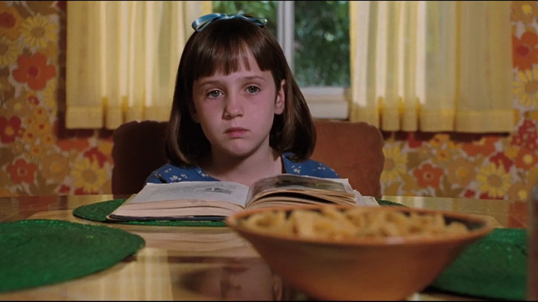 Matilda at the breakfast table with a book, looking sad, in Matilda