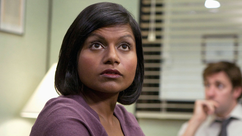 Mindy Kaling as Kelly sitting in Michael's office with Jim in the background in The Office