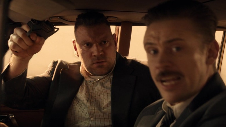 Olivier Richters' Hauke holds a gun as he sits in the passenger seat of a car alongside Boyd Holbrook's Klaber in Indiana Jones and Dial of Destiny