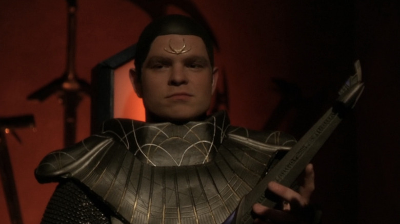 Michael Adamthwaite's Herak holds a Rod of Anguish and smiles in Stargate SG-1