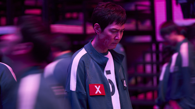 Gi-hun looking down at the ground with an X on his uniform in Squid Game season 2