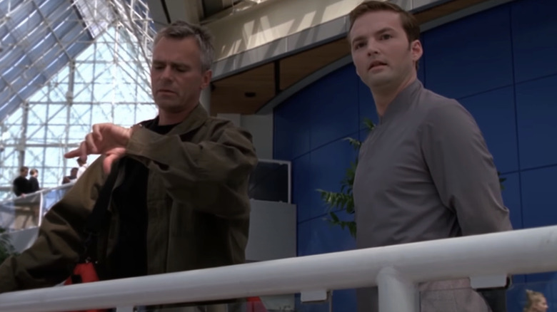 Richard Dean Anderson's Jack O'Neill looks at his watch as he stands beside Dion Luther's Mollem in Stargate SG-1