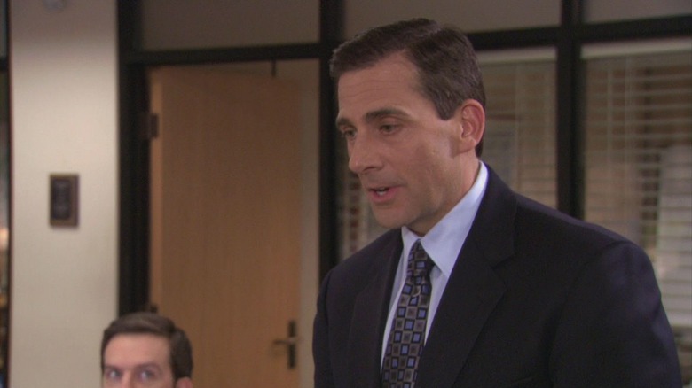 Michael Scott stands in the office as Andy look in the background of the office