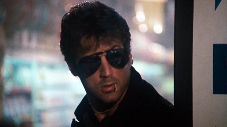 Marion Cobretti, wearing sunglasses, looks over her left shoulder in Cobra