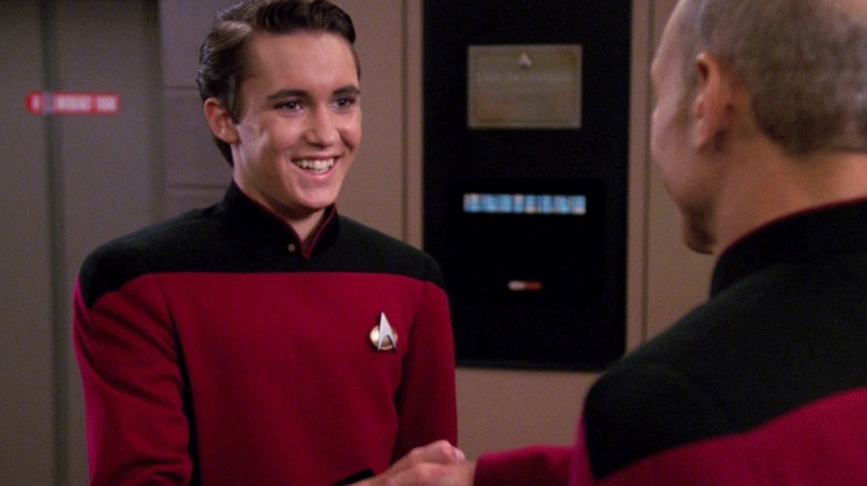 Wesley Crusher, on the bridge of the Enterprise, smiling and shaking Captain Picard's hand.