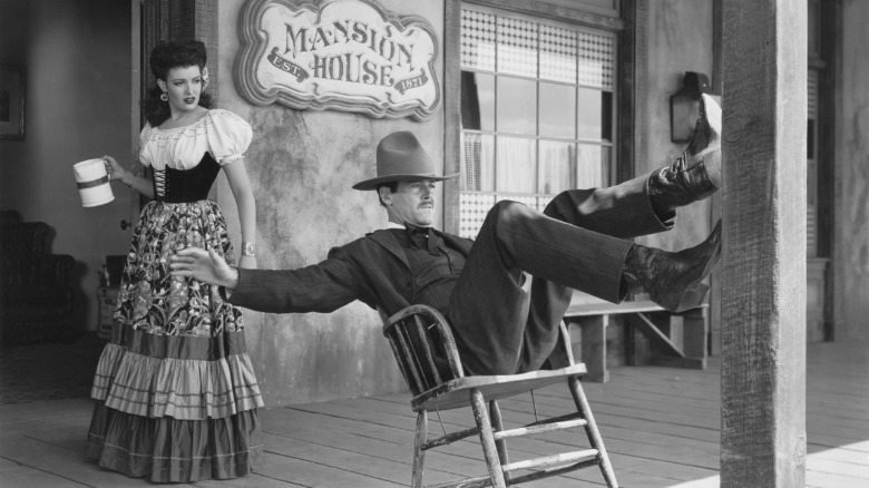 Henry Fonda as Wyatt Earp leans back in a chair on a porch while Linda Darnell as Chihuahua looks on in My Darling Clementine