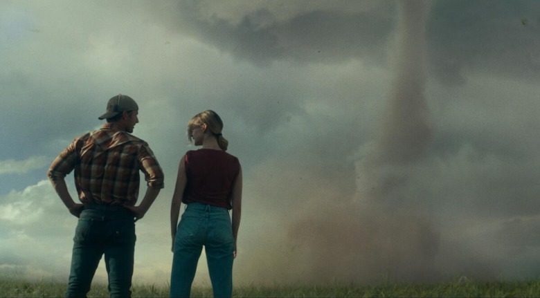 Glen Powell as Tyler and Daisy Edgar-Jones as Kate look at each other with a tornado in the background in Twisters